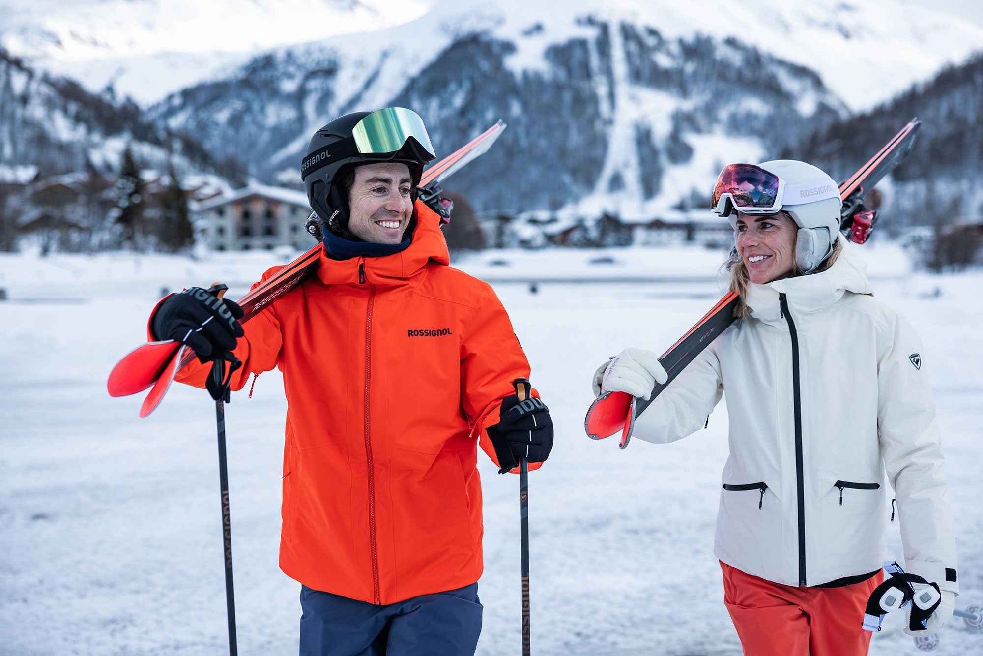 Two skiers in colorful outfits with ski equipment against a snowy mountain backdrop